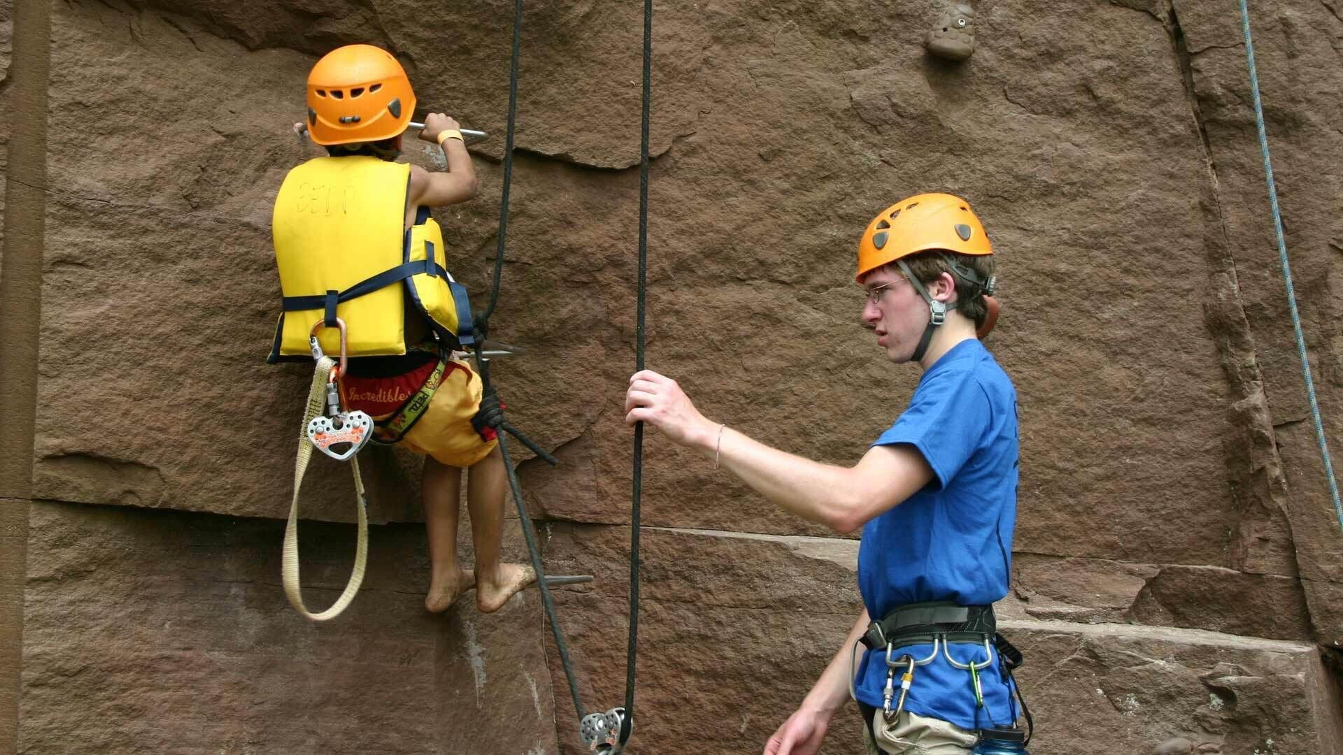 Zwei Personen beim Klettern, eine hilft der anderen.