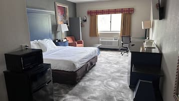 A hotel room with a bed, desk, chair, and a large window with curtains.