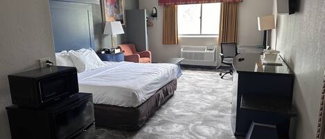 A hotel room with a bed, desk, chair, and a large window with curtains.