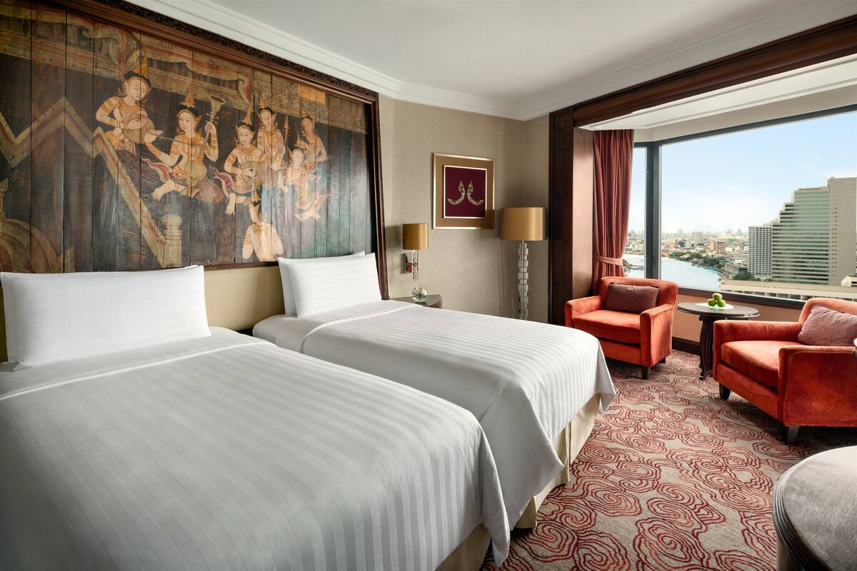 A hotel room with two beds, a large mural, a city view, and a red patterned carpet.