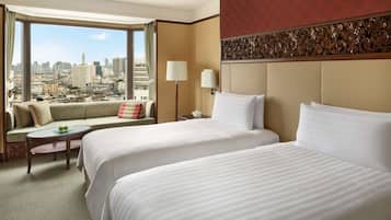 A hotel room with two beds, a sofa, a small table, and a view of a cityscape.
