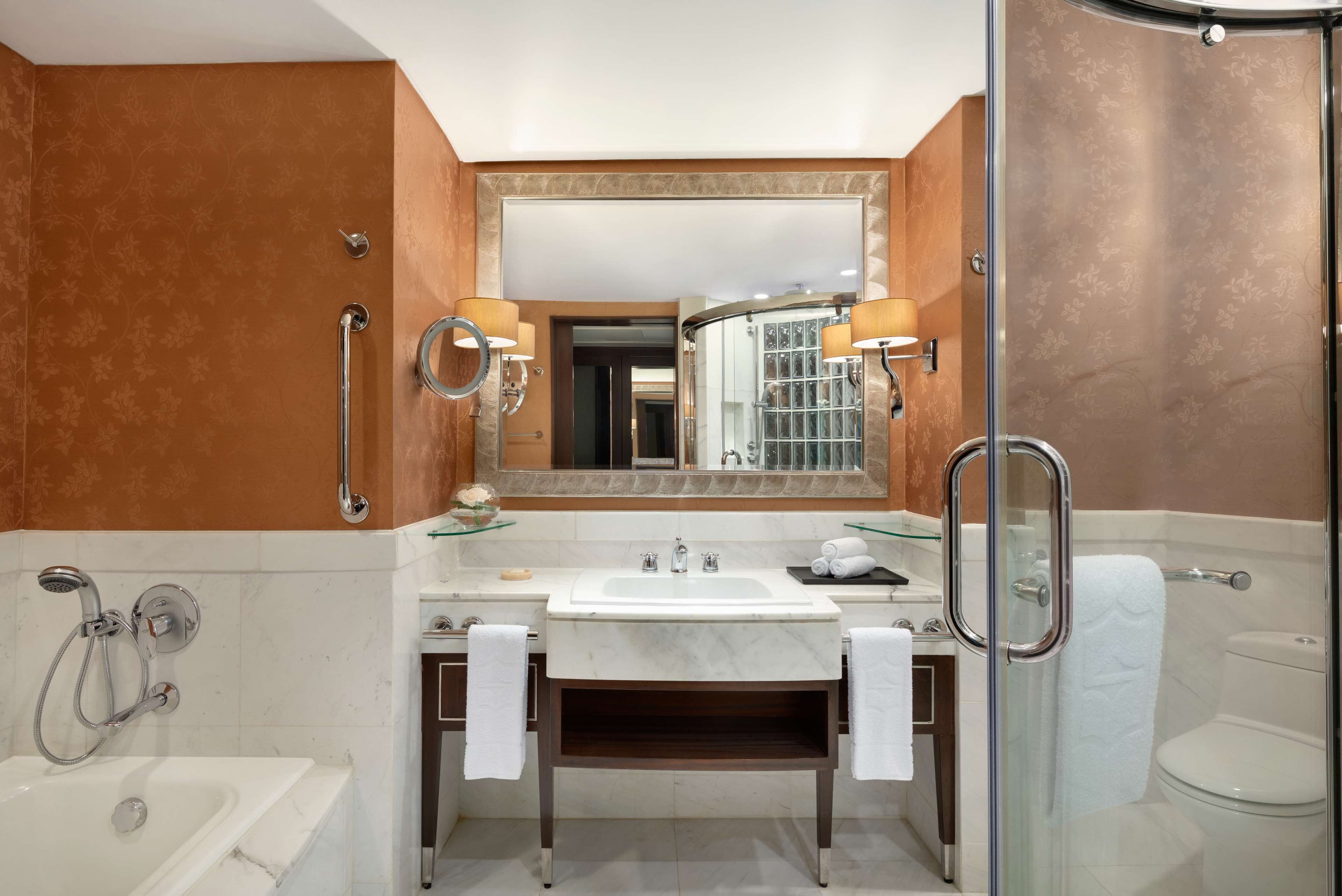Un baño moderno con bañera, ducha con mampara de vidrio, tocador con lavabo y un espejo grande.