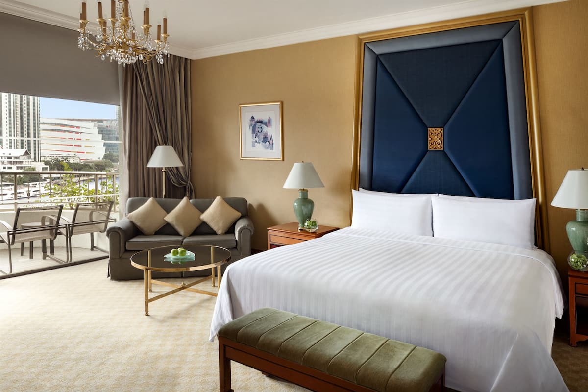 A hotel room with a large bed, a sofa, a round table, and a view of the city.