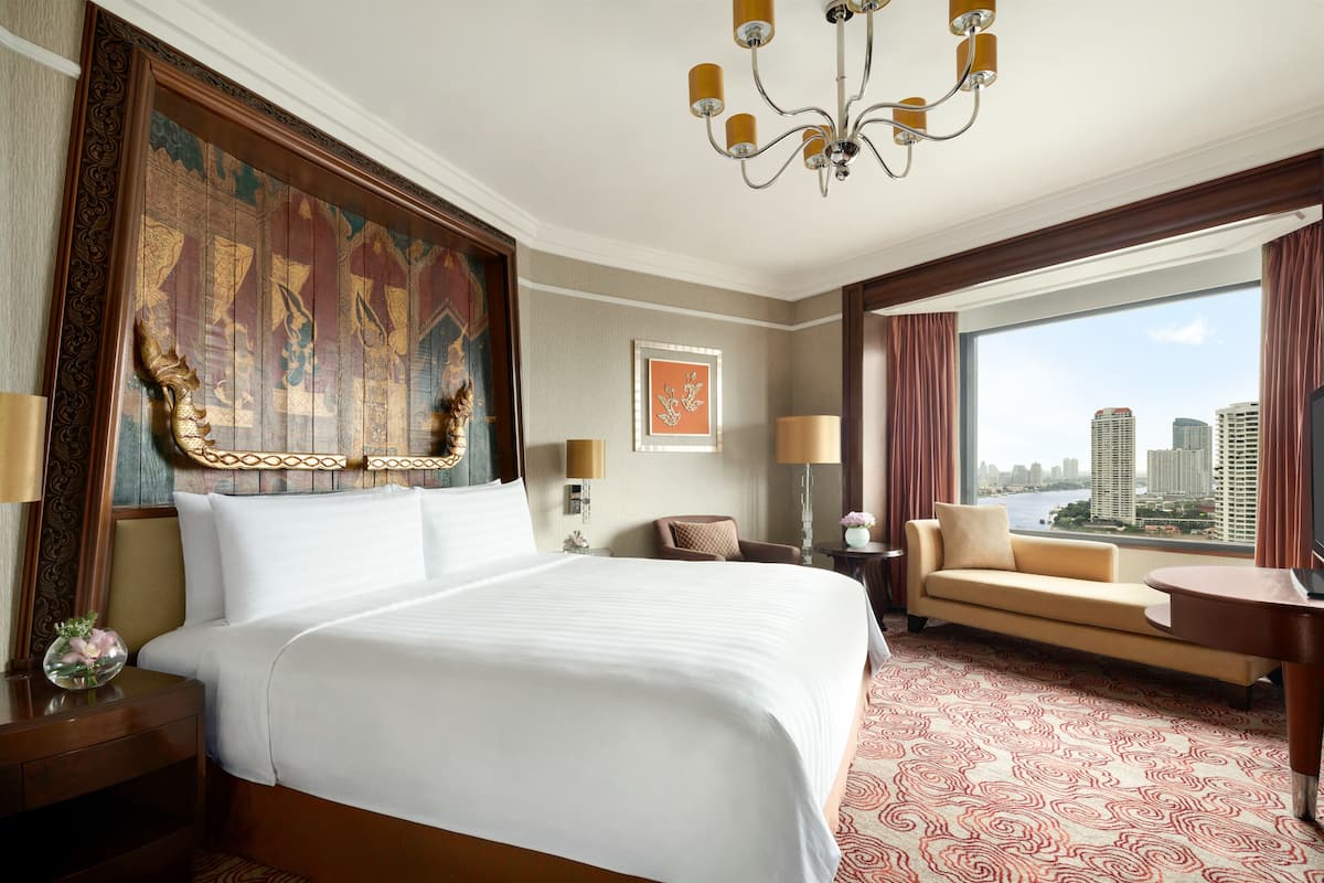 A hotel room with a large bed, a sofa, a view of the city, and a chandelier.