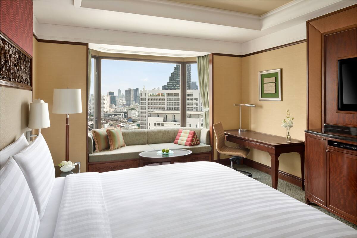 A hotel room with a large bed, a sofa with a city view, a desk, and a television.