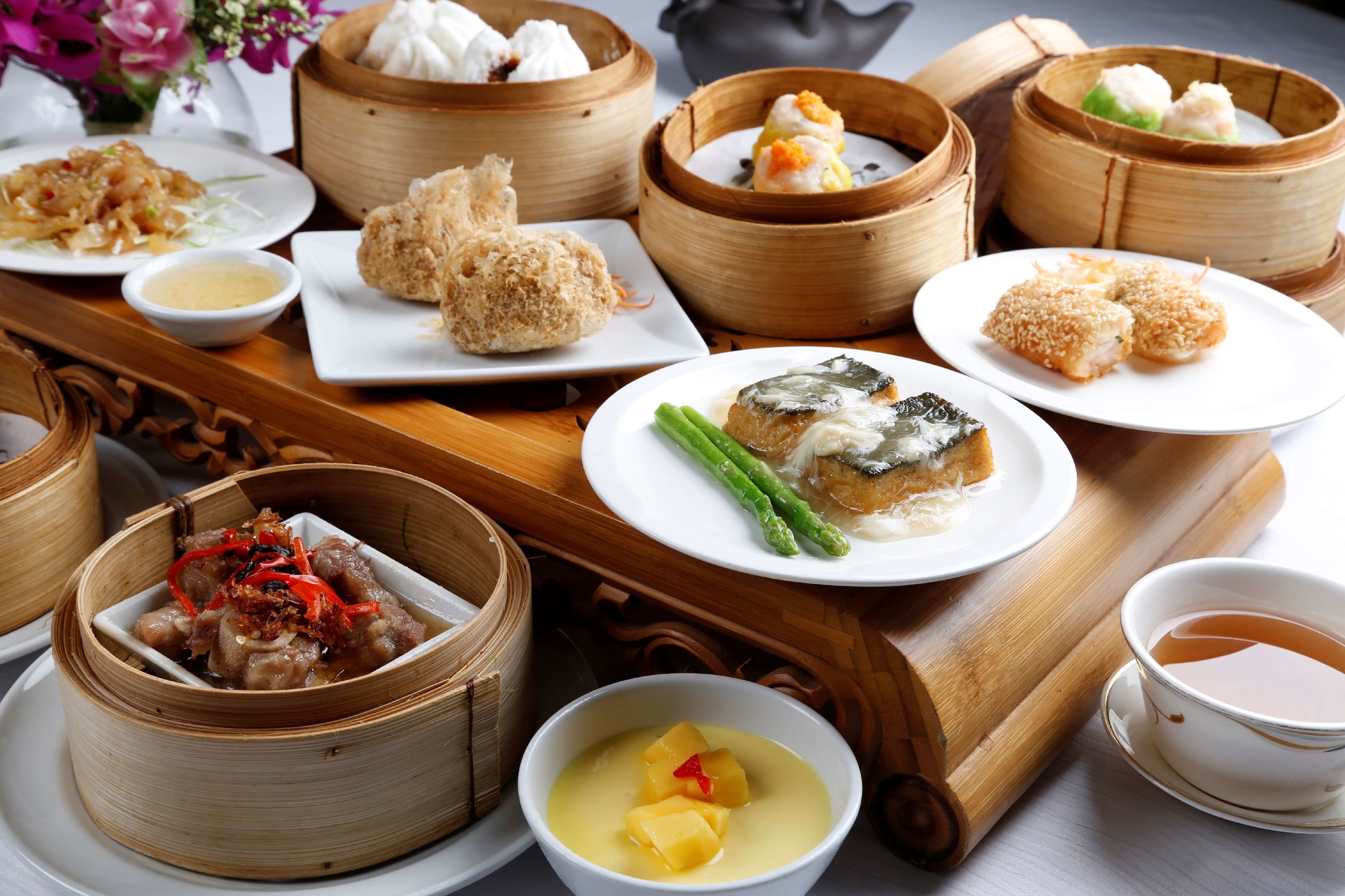 Variedad de platos asiáticos, como dim sum y un tazón de sopa con fruta.