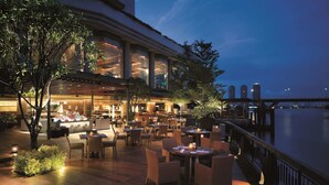 An outdoor dining area with tables and chairs, a poolside view, and a building with large windows.