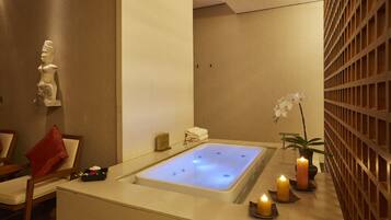 A spa room with a bathtub, a statue, a chair, and candles.