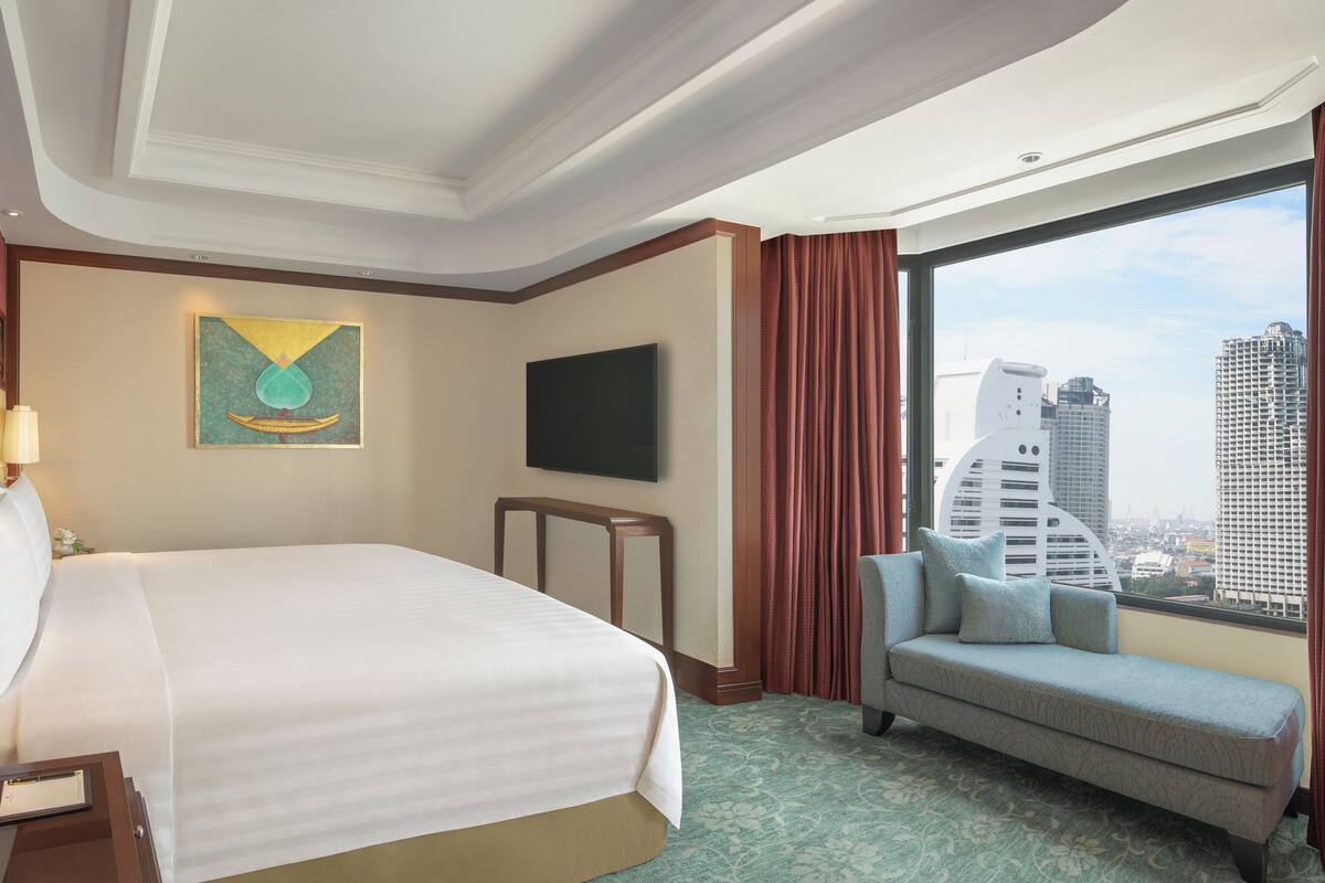 A hotel room with a large bed, a sofa, a TV, and a city view.