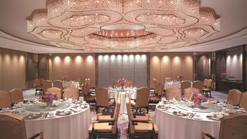 Uma sala de jantar formal com mesas redondas, cadeiras e um lustre grande.