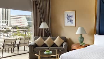 A hotel room with a large bed, a sofa, a coffee table, and a view of the cityscape.