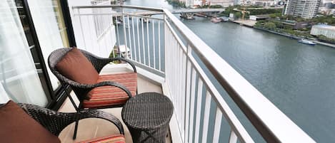 A balcony with wicker furniture overlooking a river and cityscape.