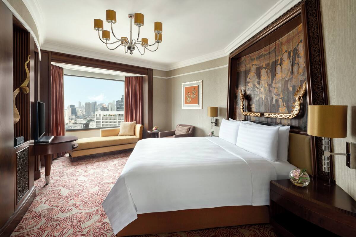 A hotel room with a large bed, a sofa, a TV, and a view of the city skyline.
