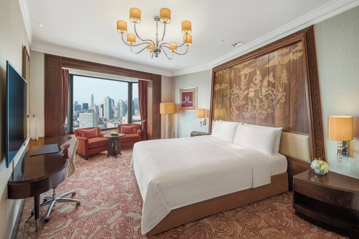 A hotel room with a large bed, a desk, a chair, a TV, and a city view.