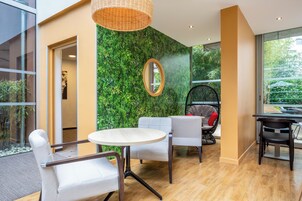Un intérieur moderne avec une table ronde, deux chaises, un luminaire suspendu en osier et un mur vert agrémenté d’un miroir.
