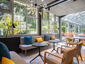 A modern interior with large windows, a glass ceiling, a sofa with cushions, and a round table. - Ibis Paris Meudon Velizy (Meudon)