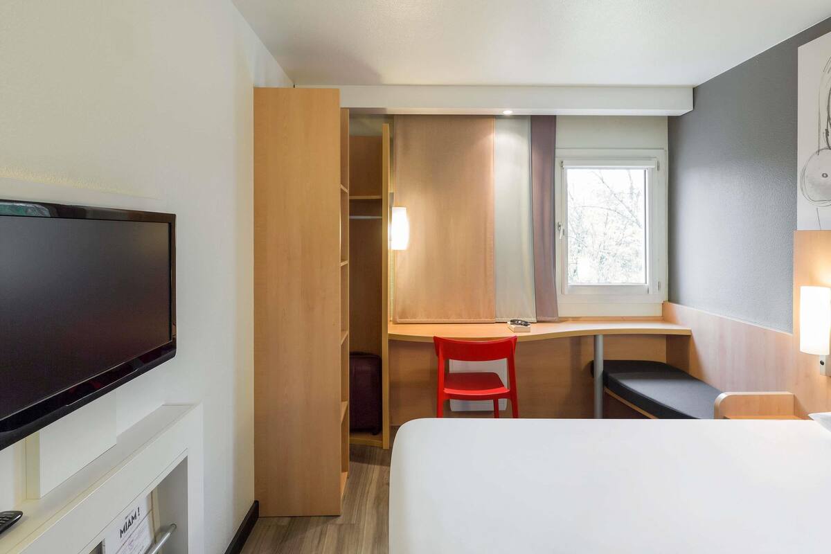 A hotel room with a bed, a desk, a TV, a wardrobe, and a window.