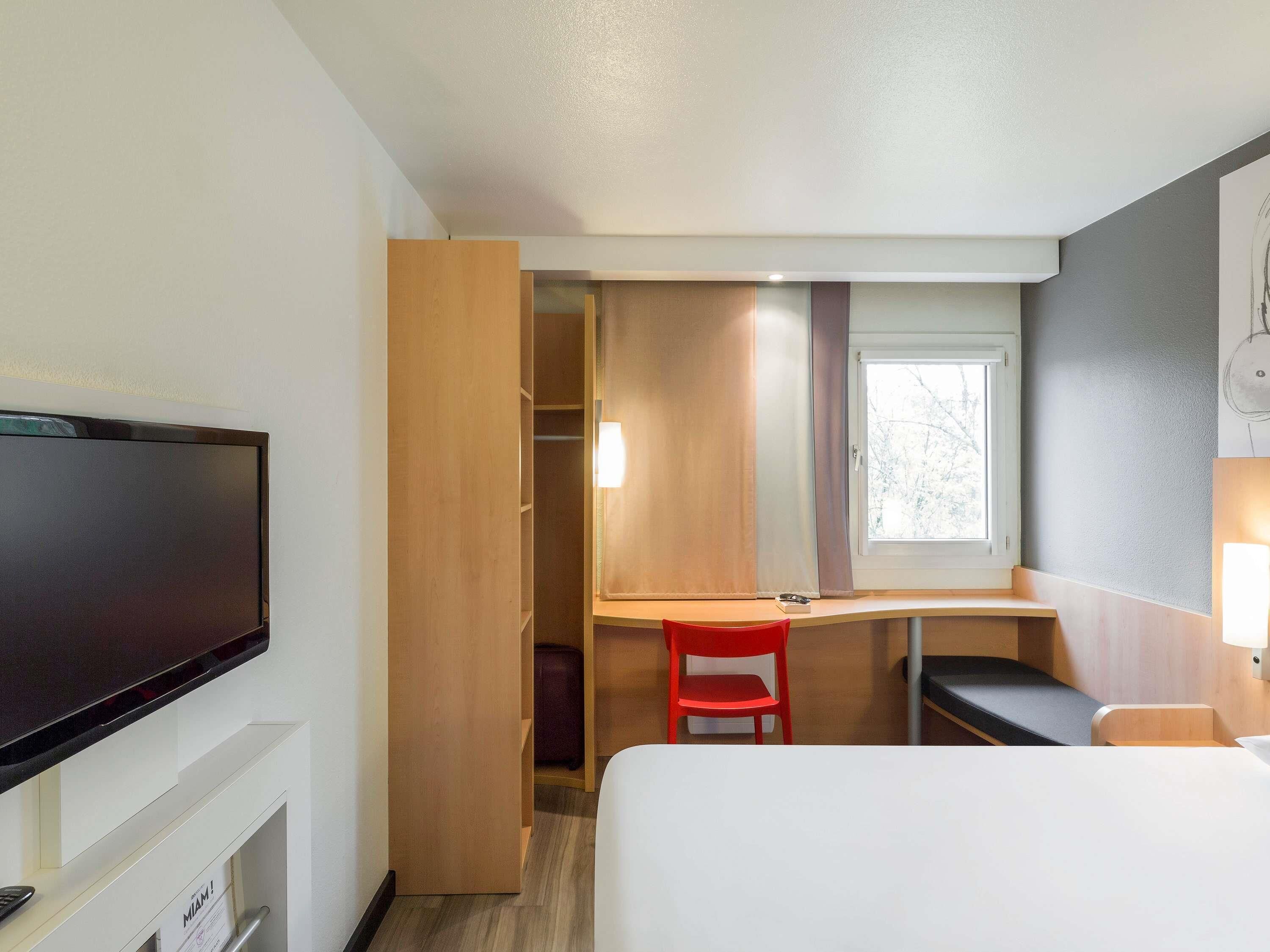 A hotel room with a bed, a desk, a TV, a wardrobe, and a window.