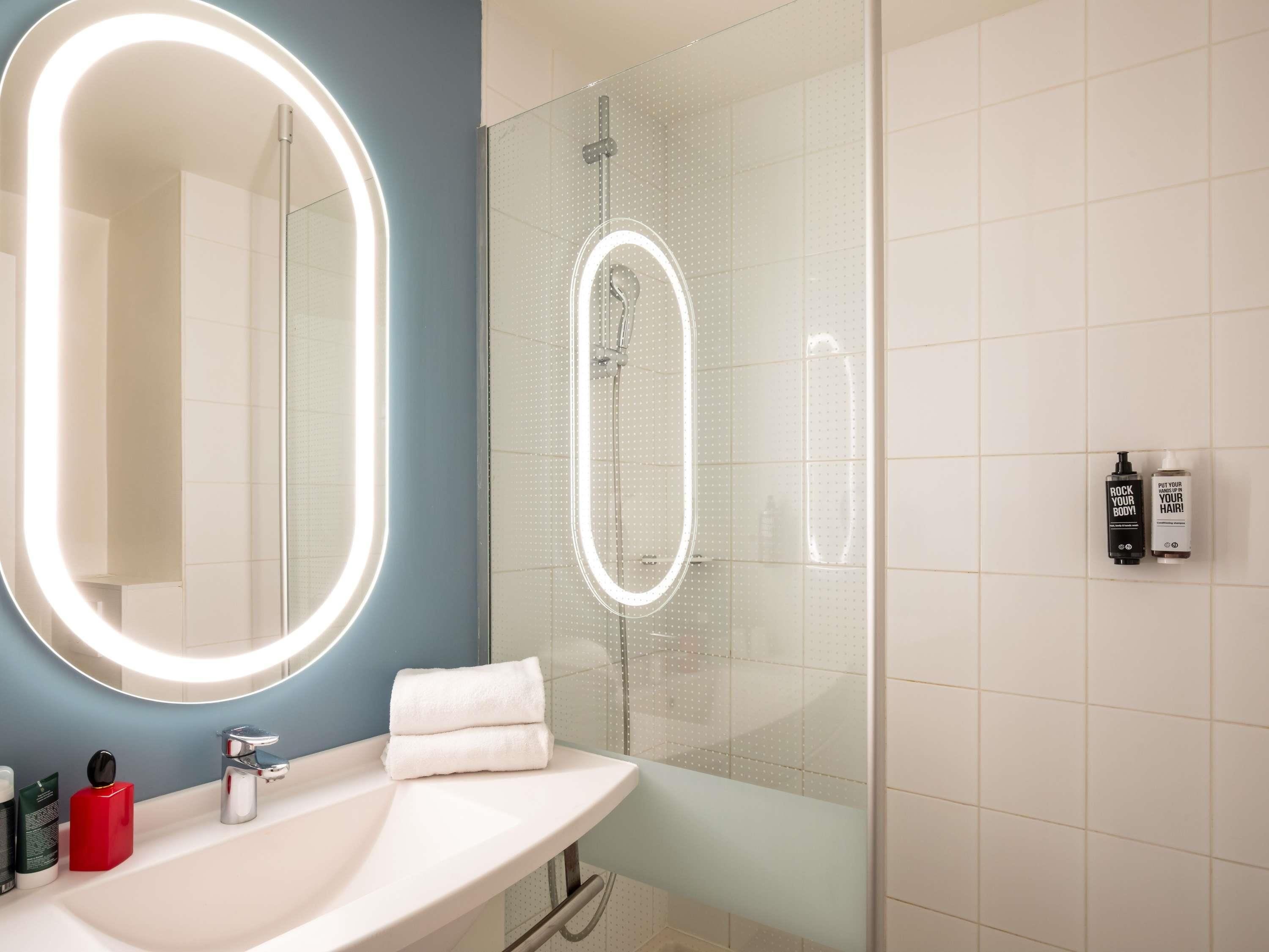 A modern bathroom with a large mirror, a glass-enclosed shower, and a white sink.