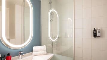 A modern bathroom with a large mirror, a glass-enclosed shower, and a white sink.