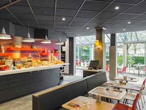 A modern restaurant interior with a central counter, seating area, and large windows. - Ibis Paris Meudon Velizy (Meudon)