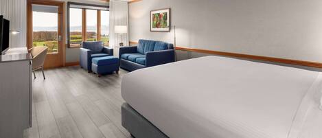 A hotel room with a large bed, a desk with a chair, two armchairs, a TV, and a window with a view of the outdoors.