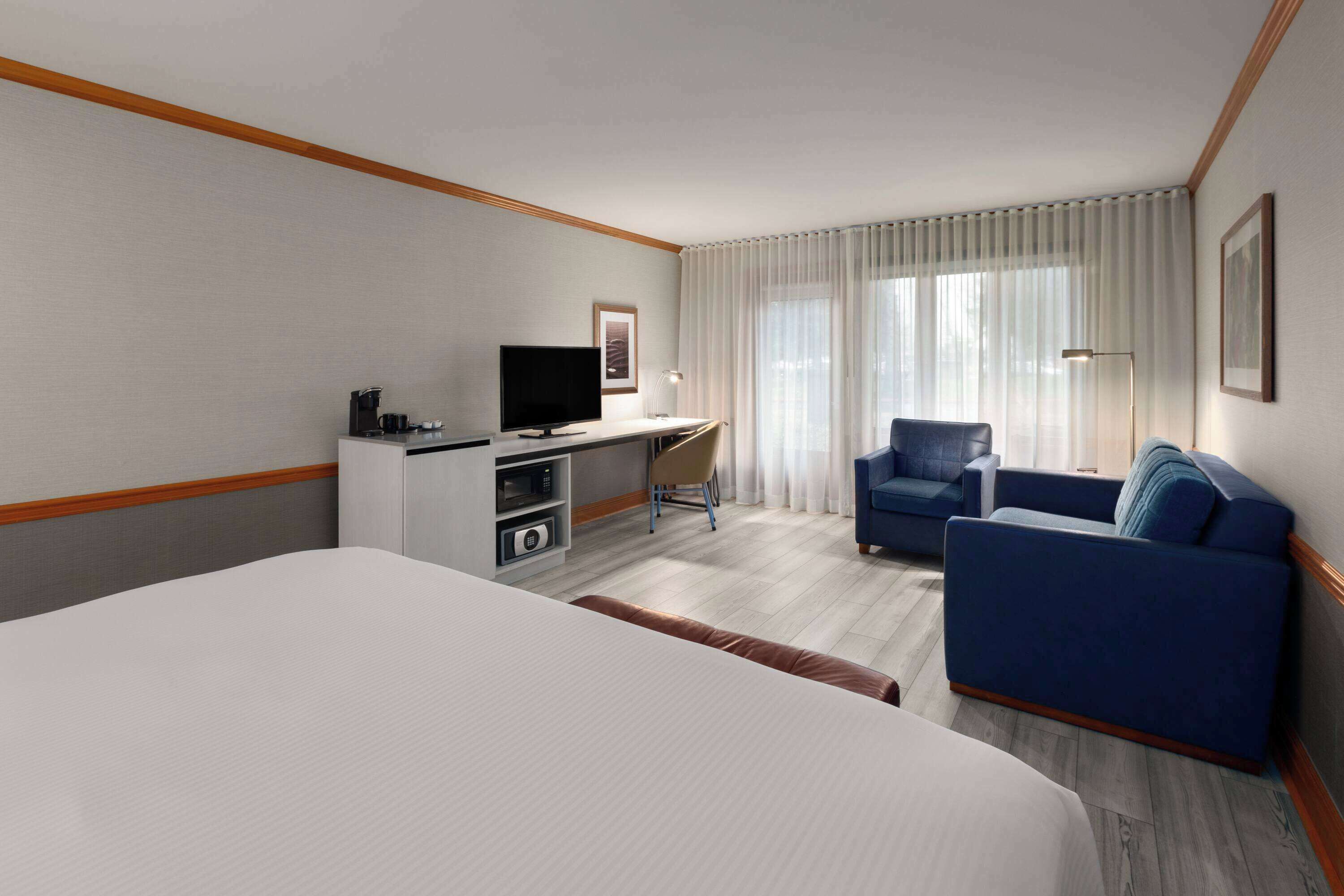 A hotel room with a large bed, a desk with a TV, a chair, and a sofa.