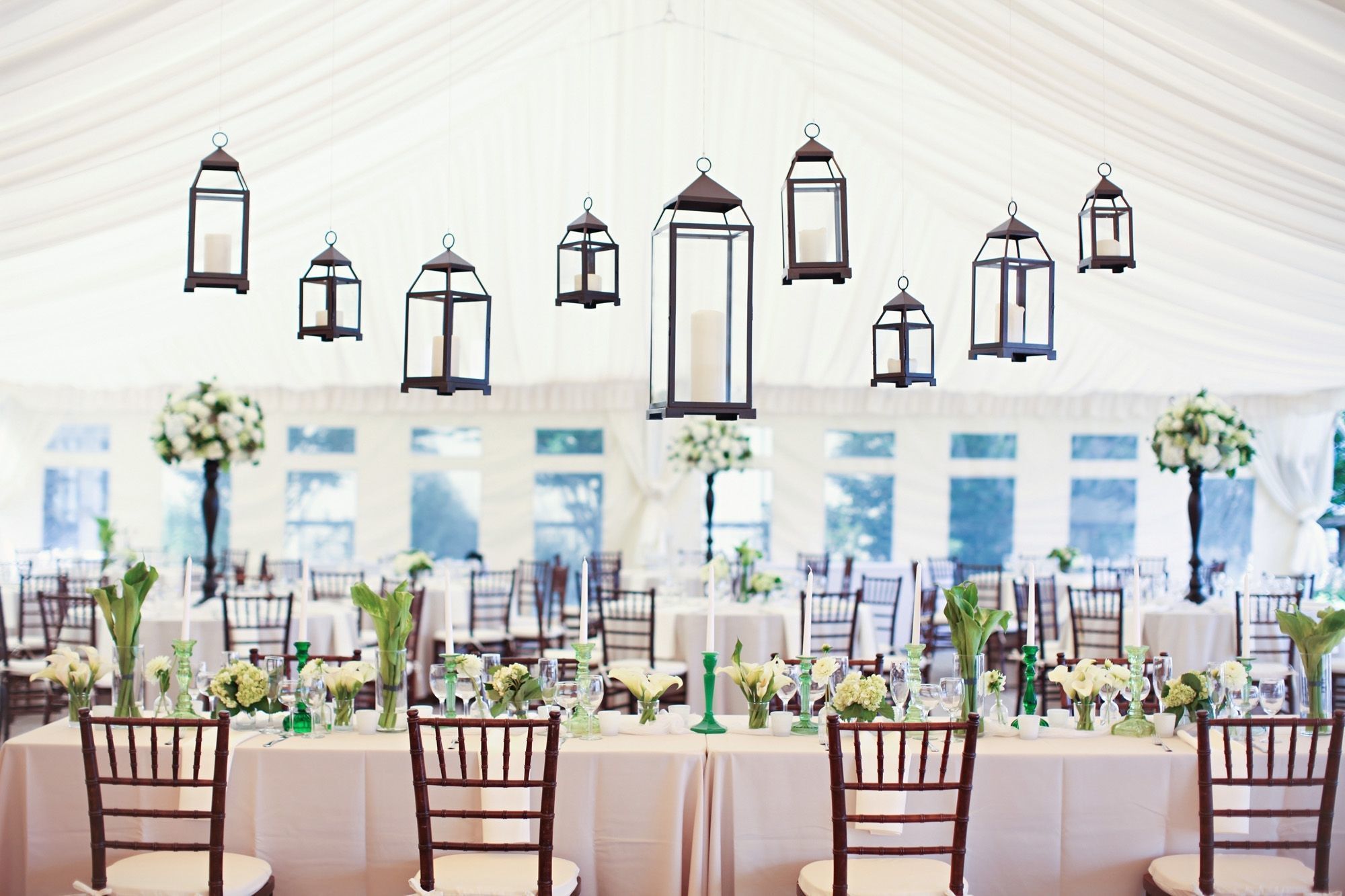 A tented event space with tables set for dining, adorned with floral centerpieces and hanging lanterns.