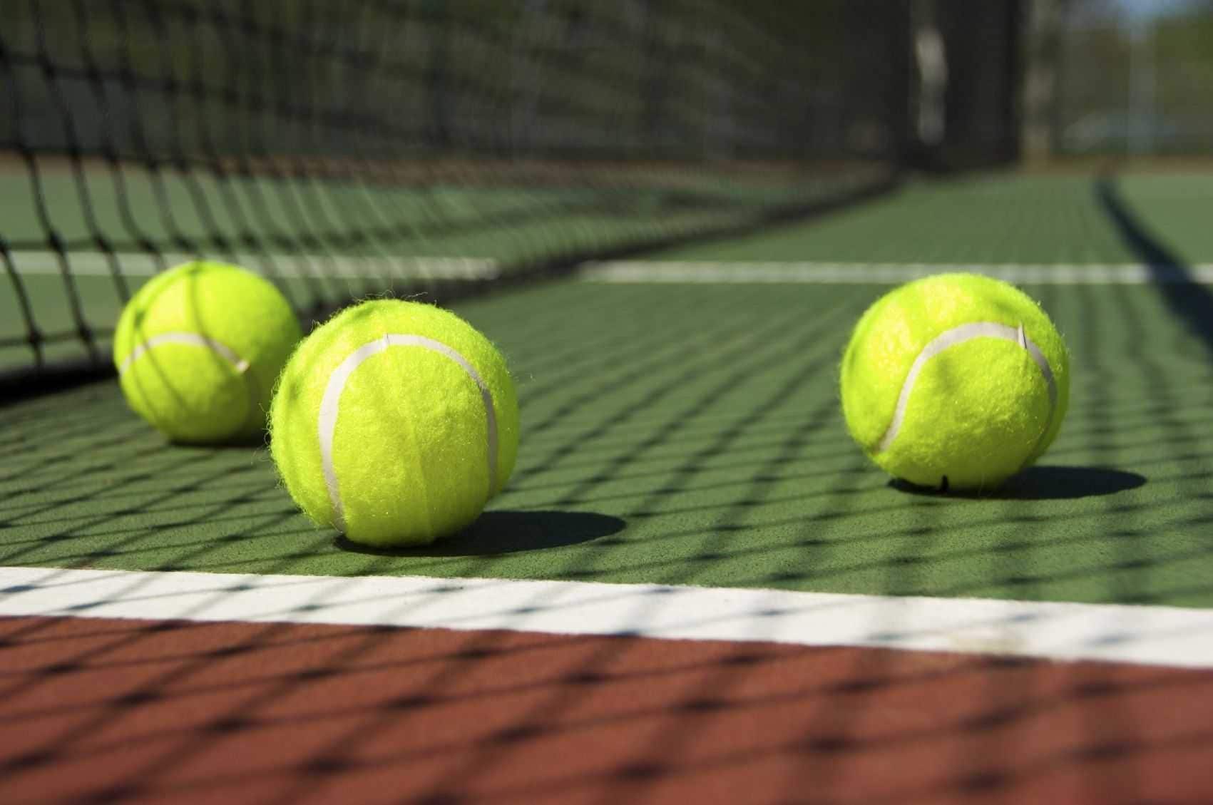 Three tennis balls on a tennis court with a net.
