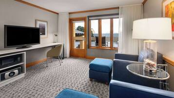 Hotelkamer met een flatscreen televisie, een bureau, een stoel, een bank, een klein tafeltje met een lamp, en uitzicht op de omgeving via een schuifdeur.