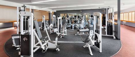 Un gimnasio con diversas máquinas de ejercicio, espejos y suelo alfombrado.