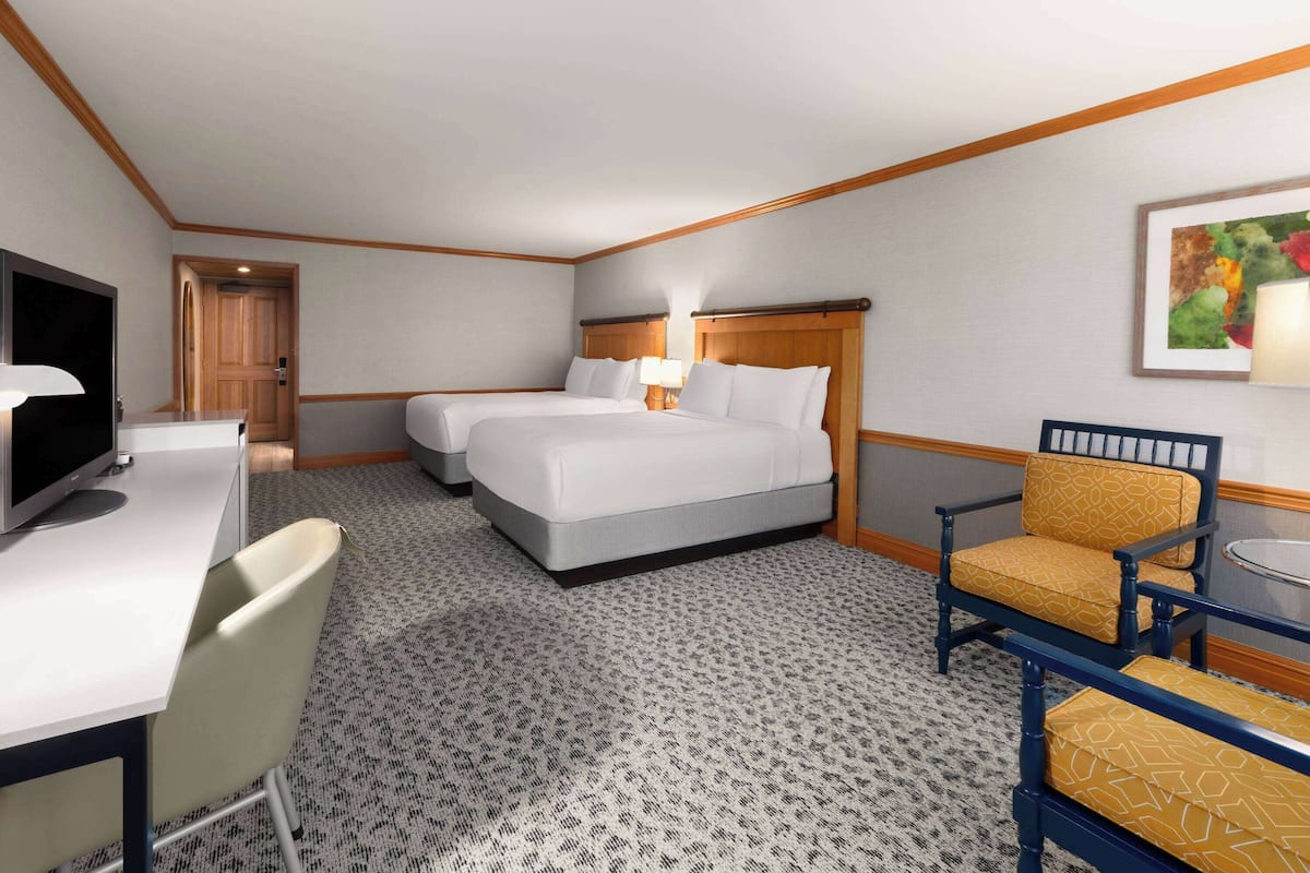 A hotel room with two beds, a desk with a computer, a chair, and a small table with a lamp.