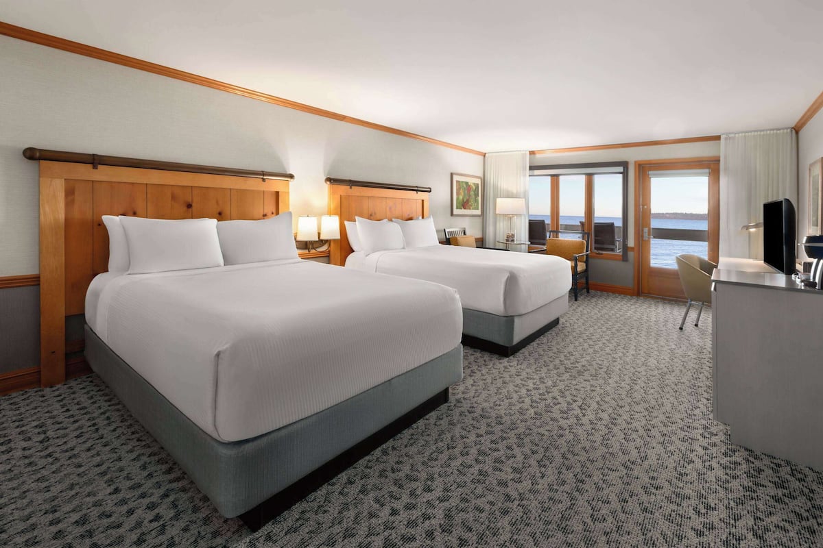 A hotel room with two beds, a desk, a chair, and a large window with a view of the sea.