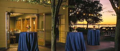 An outdoor dining area with tables covered in blue tablecloths, a brick pathway, and string lights.