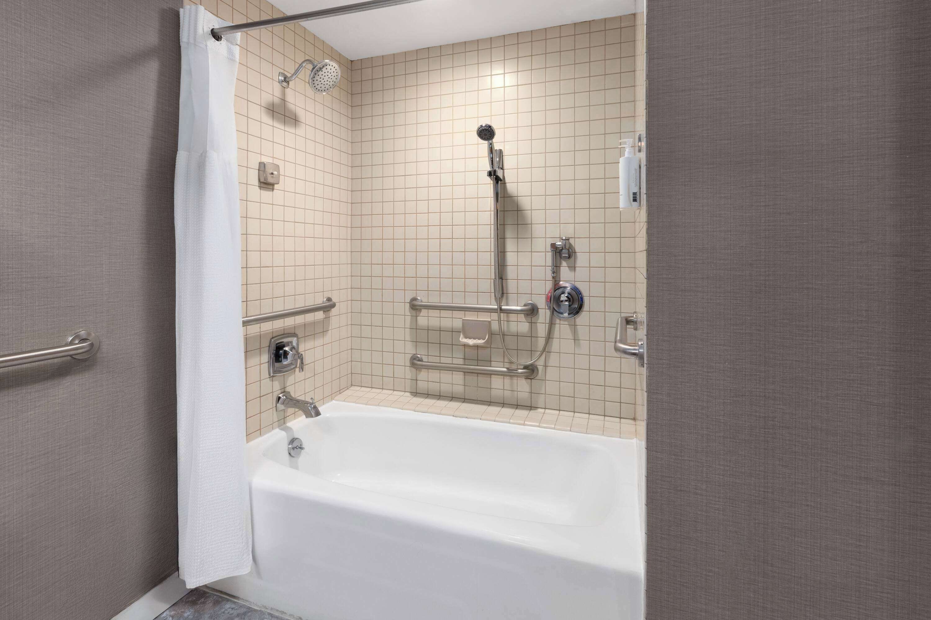 A modern bathroom with a bathtub, shower, and grab bars.