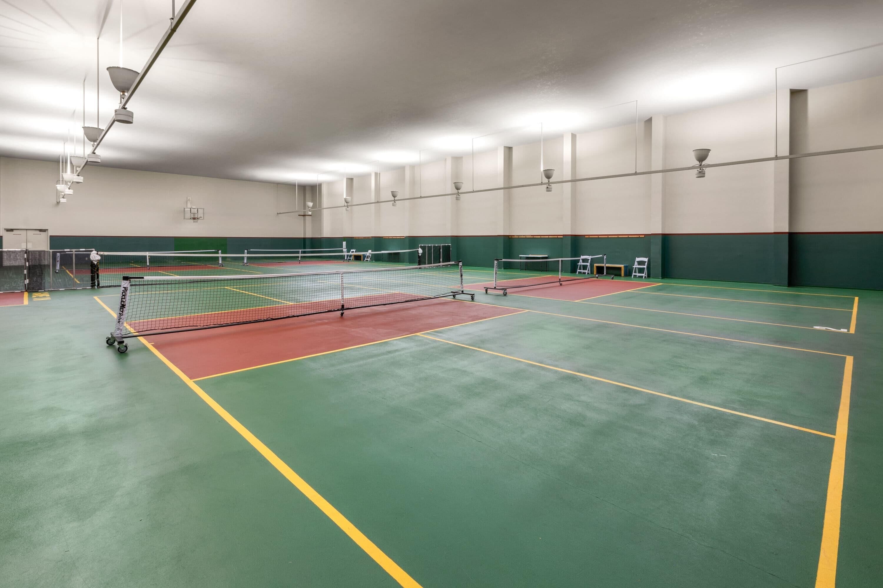 Un court de tennis intérieur doté de plusieurs terrains, d’un filet et d’un système d’éclairage.
