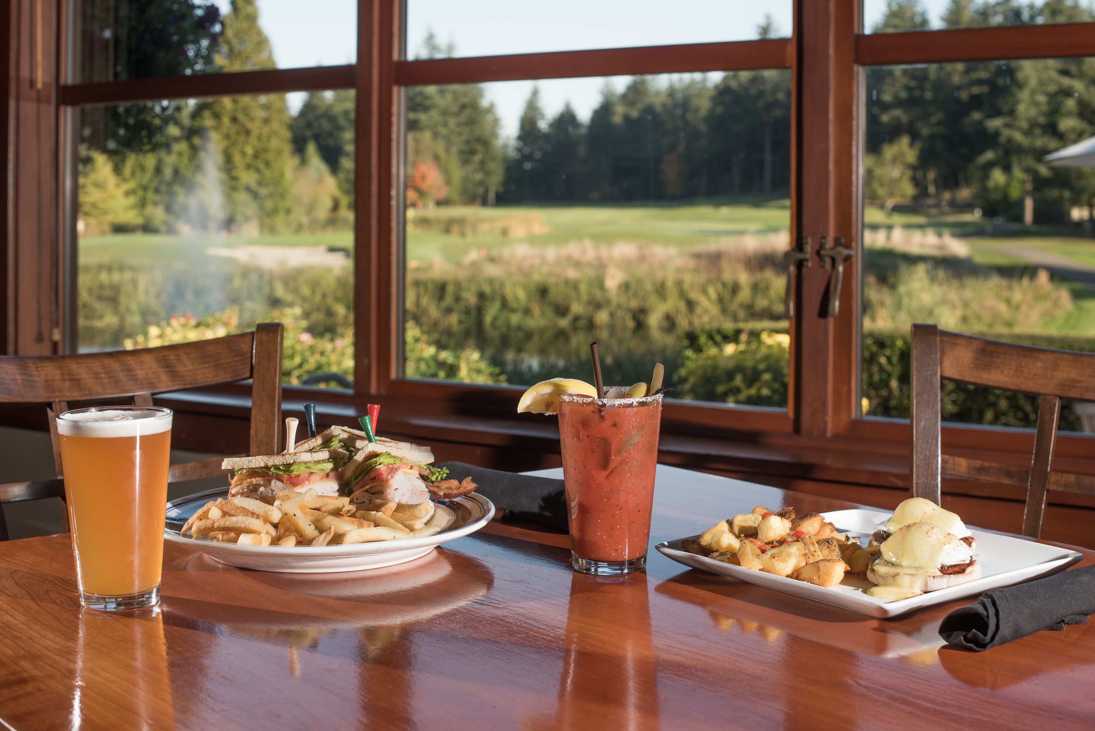 A table with a meal consisting of a sandwich, fries, and a drink, set against a backdrop of a scenic view through large windows.
