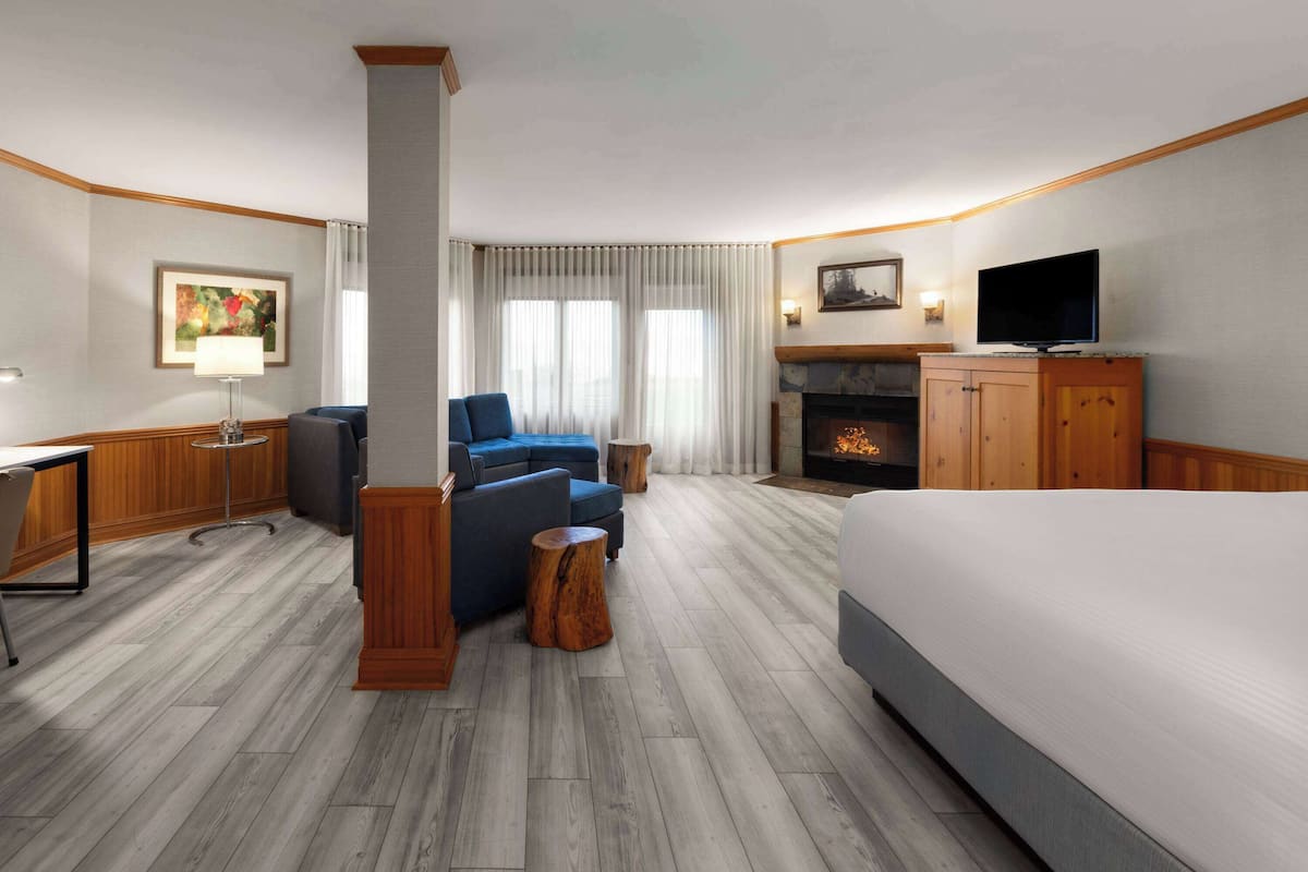 A hotel room with a bed, a TV, a fireplace, a sofa, and a desk.