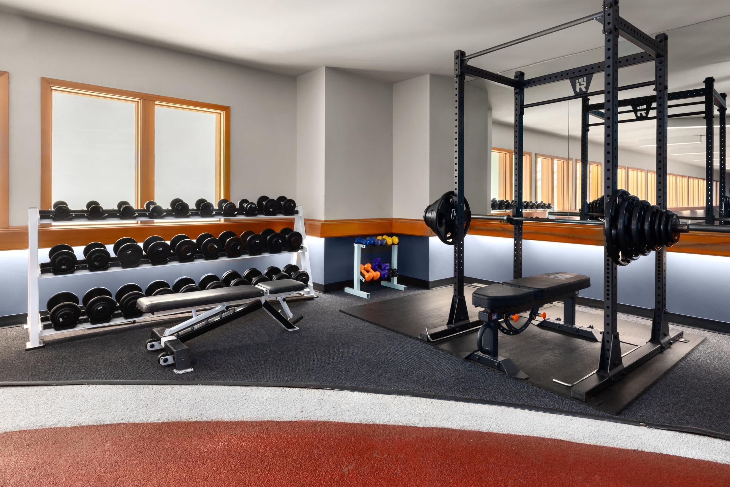 Een sportschool met gewichthefapparatuur, dumbbells en een bank.