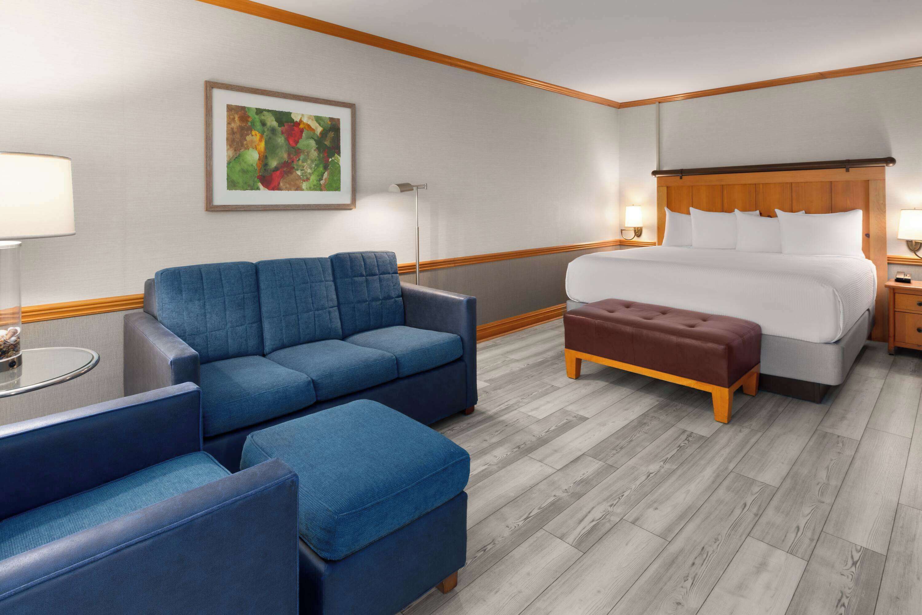 Een hotelkamer met een bed, een blauwe bank, een poef, een kleine tafel en een vloerlamp.