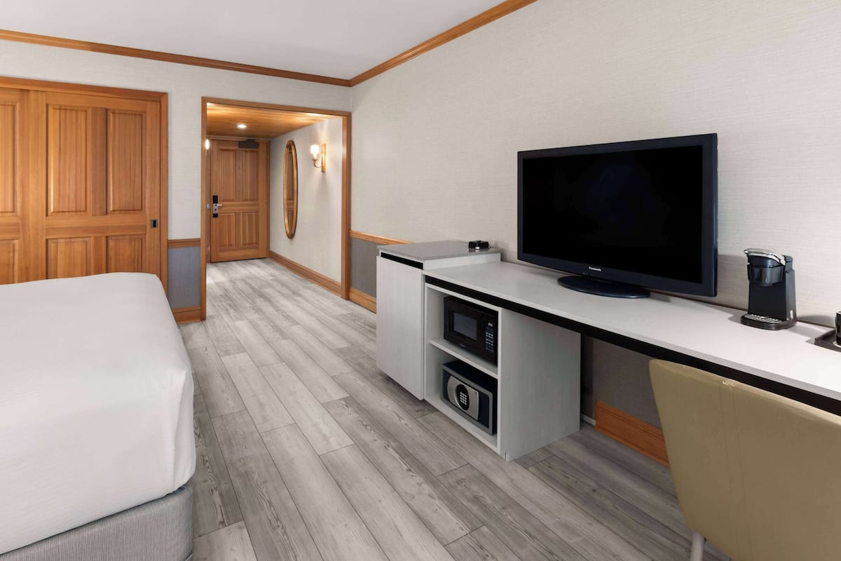 A hotel room with a bed, a desk with a television, a microwave, and a coffee maker.