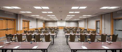 A large conference room with multiple tables and chairs, equipped with water glasses and nameplates.