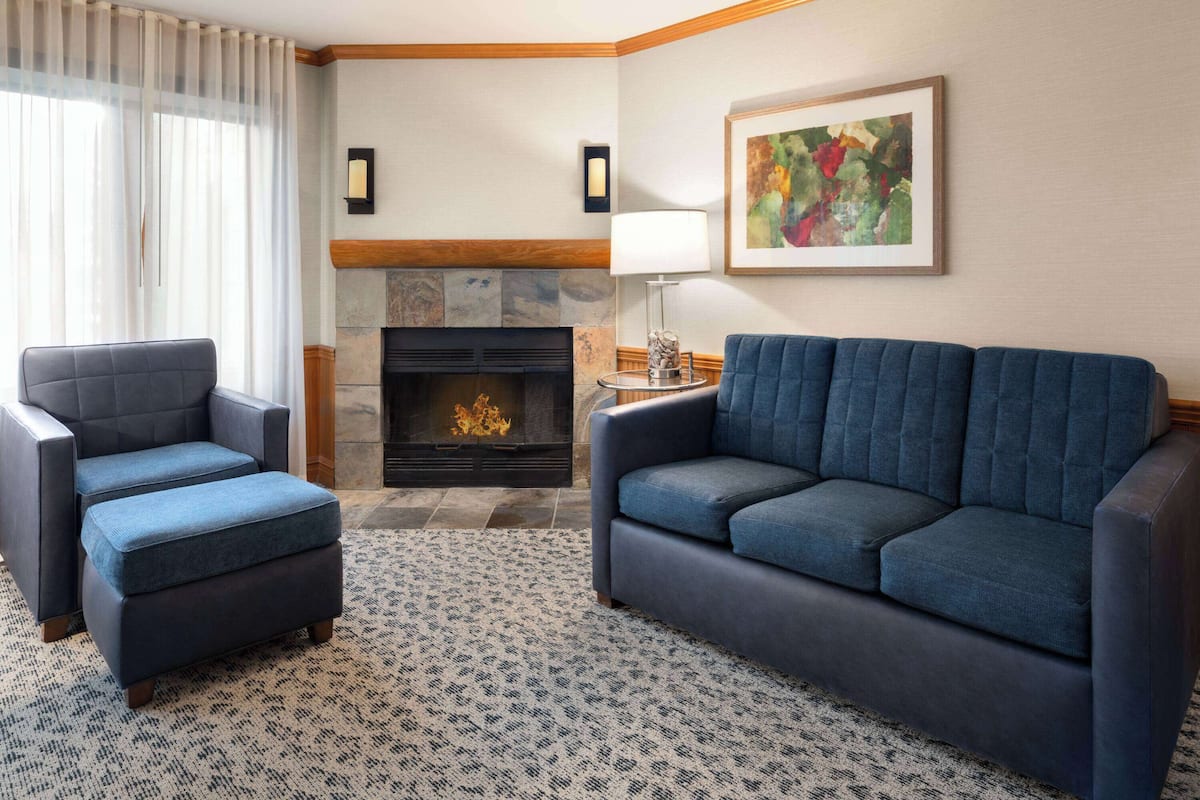 A living room with a fireplace, two armchairs, a sofa, a patterned rug, and a painting on the wall.