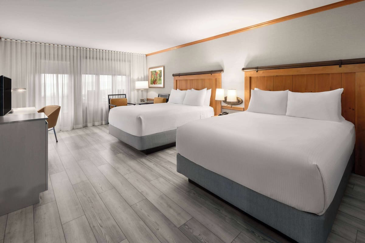 A hotel room with two beds, a desk, a chair, and a TV.