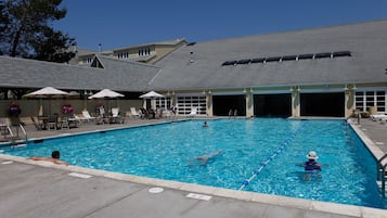 En swimmingpool med solstolar och parasoller, ett takförsett område och en byggnad med en garageuppfart.