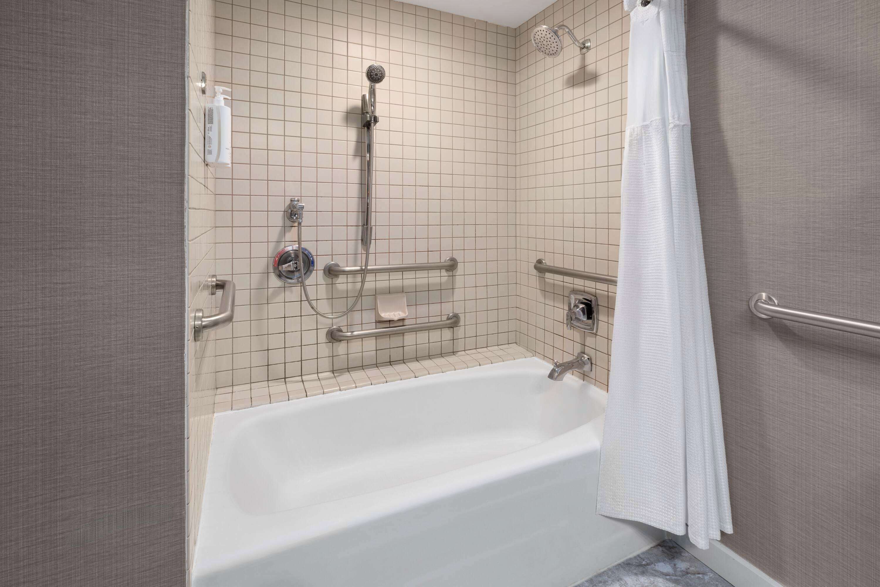 Un baño con bañera, barras de apoyo, cabezal de ducha y un perchero para toallas.