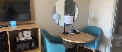 A hotel room with a TV, microwave, and a small table with chairs.
