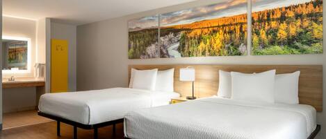 A hotel room with two beds, a wooden headboard, a painting of a forest, and a small desk with a lamp.