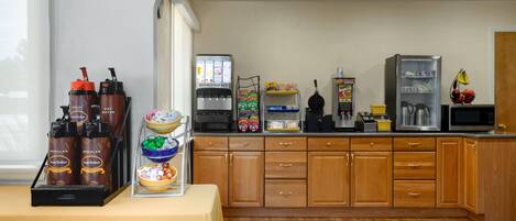 Una cocina con estación de café, microondas, refrigerador y diversos alimentos.