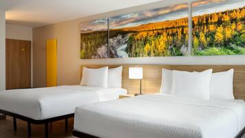 A hotel room with two beds, a wooden headboard, a large painting of a forest, and a bedside table with a lamp.